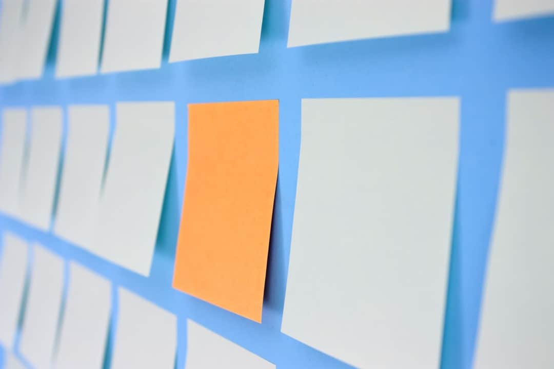 Sticky notes on a wall with one a standout, bright yellow compared to the others which are white. This signifies keeping your message straightforward and to the point in your online learning environment.
